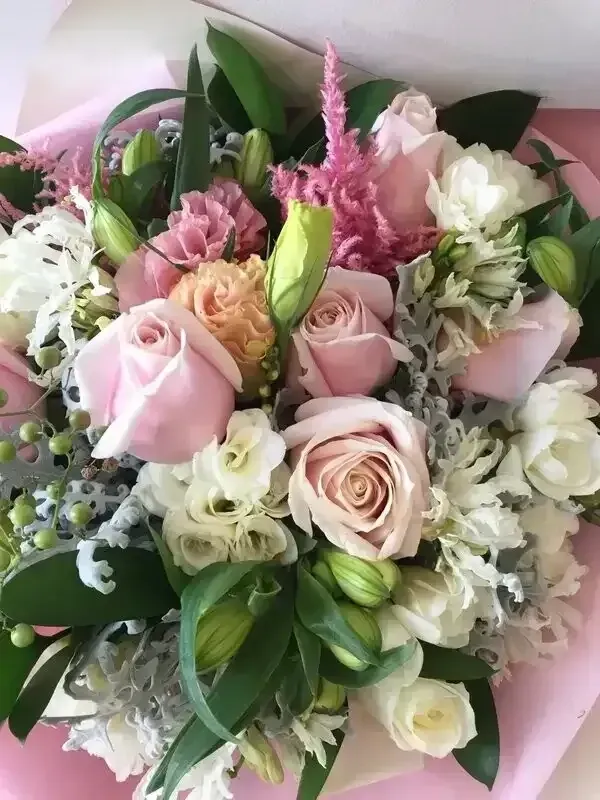 Bouquet of light pink and white flowers, with green foliage, wrapped in pink paper.