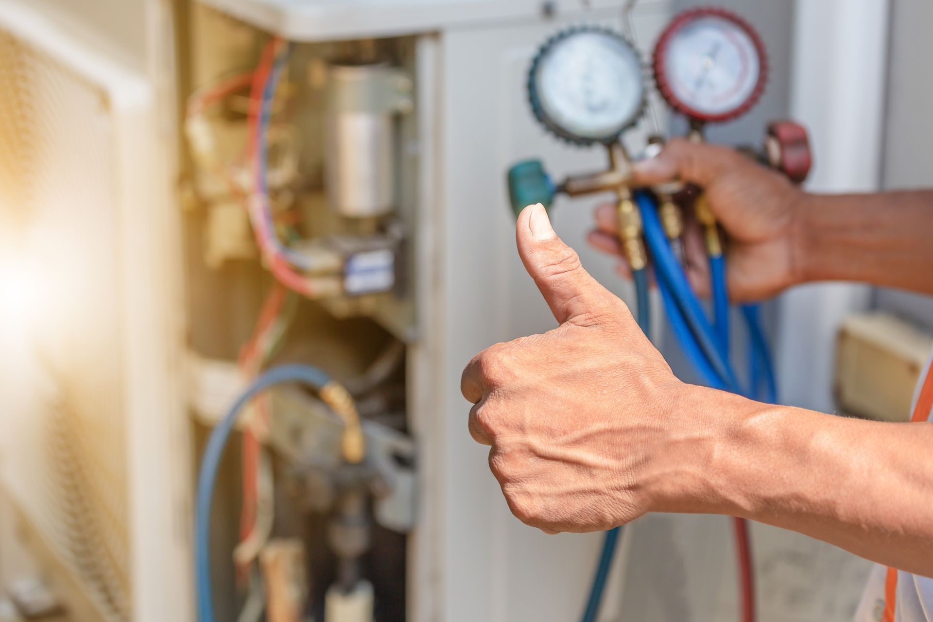 HVAC technician with thumbs up, holding gauges connected to an air conditioning unit.