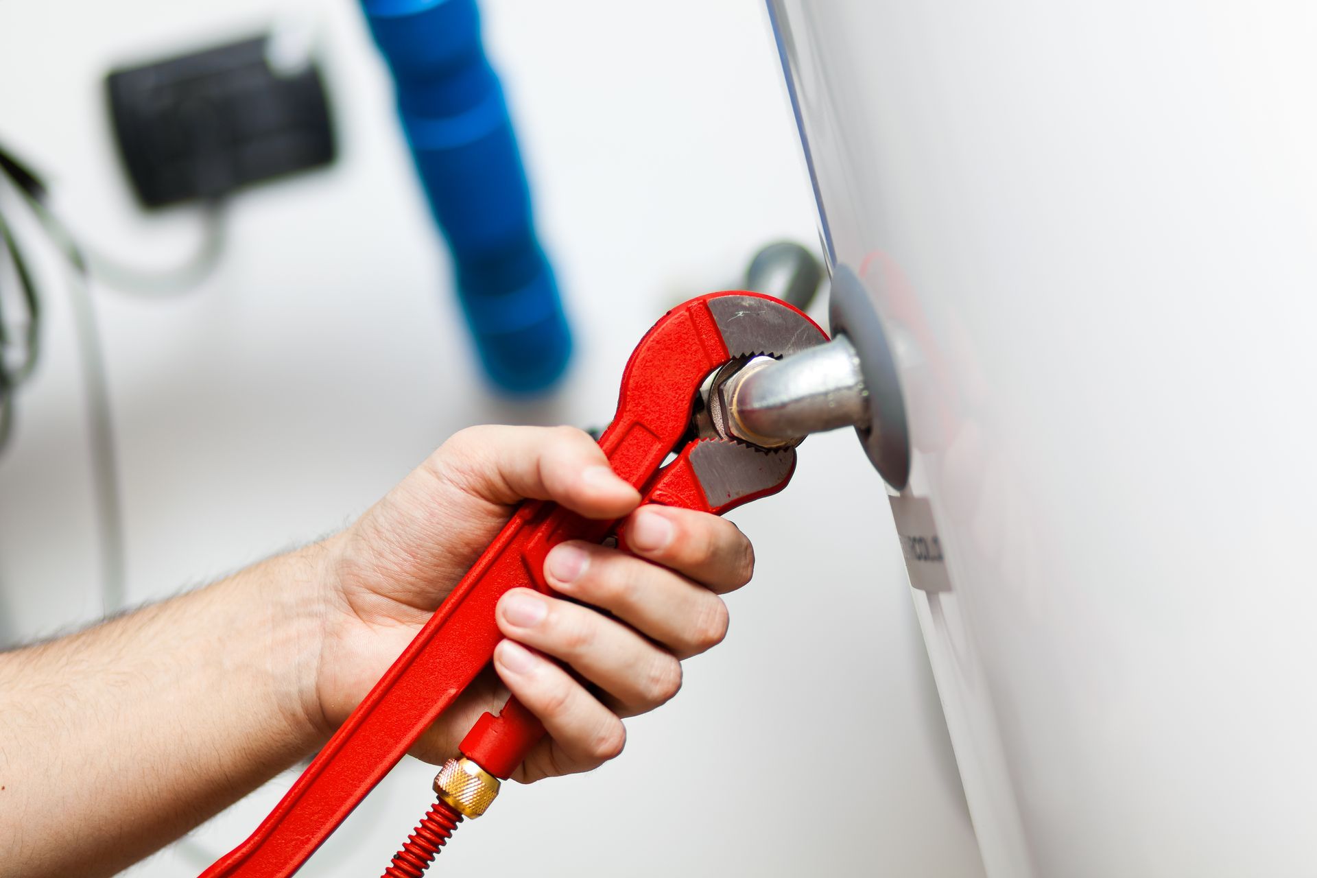 A hand using a red adjustable wrench on a metal pipe attached to a white appliance.