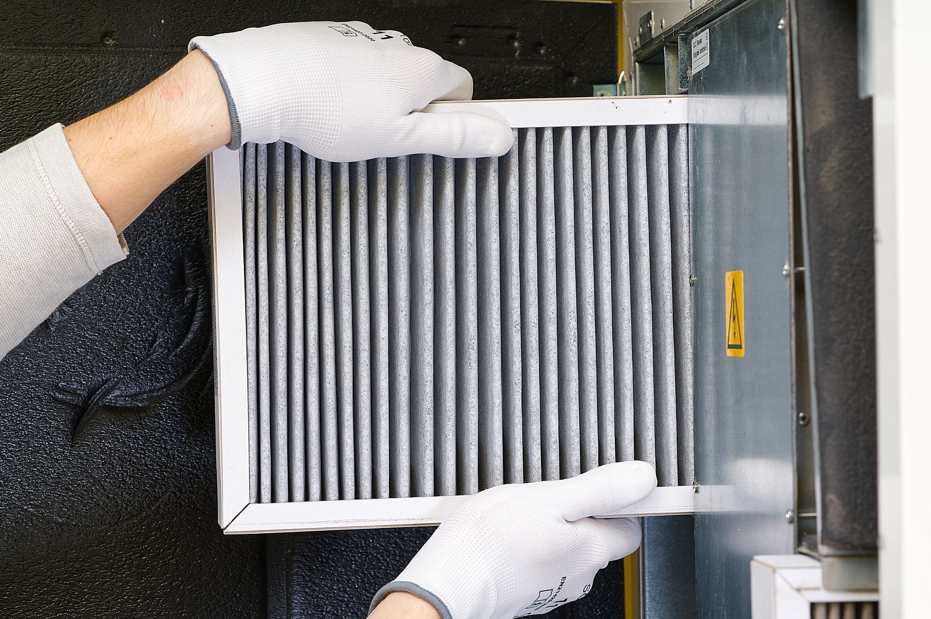 Person wearing gloves replacing a dirty air filter in a machine.