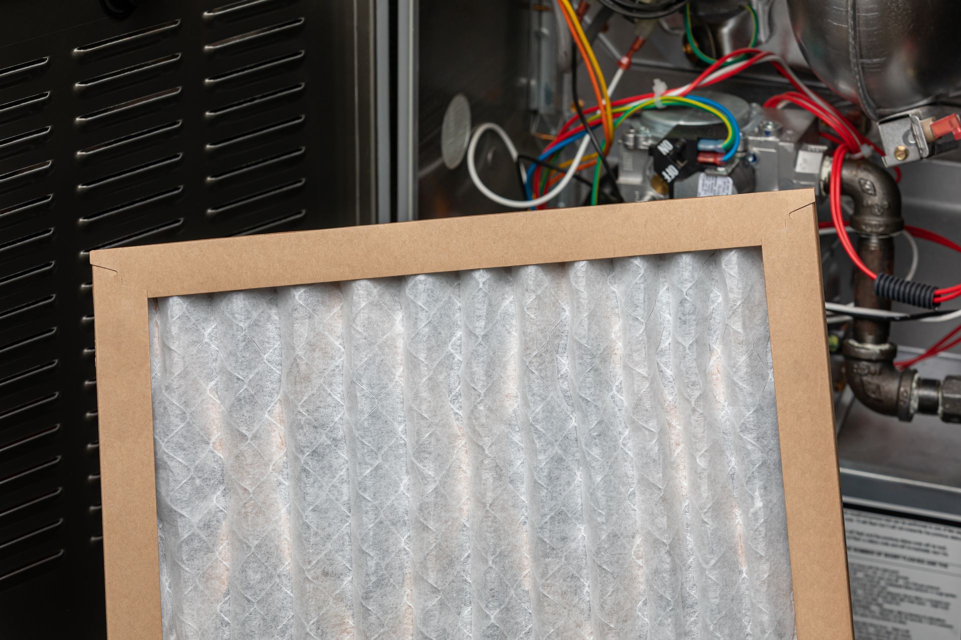 Furnace air filter being replaced, cardboard frame, pleated filter, open furnace visible.