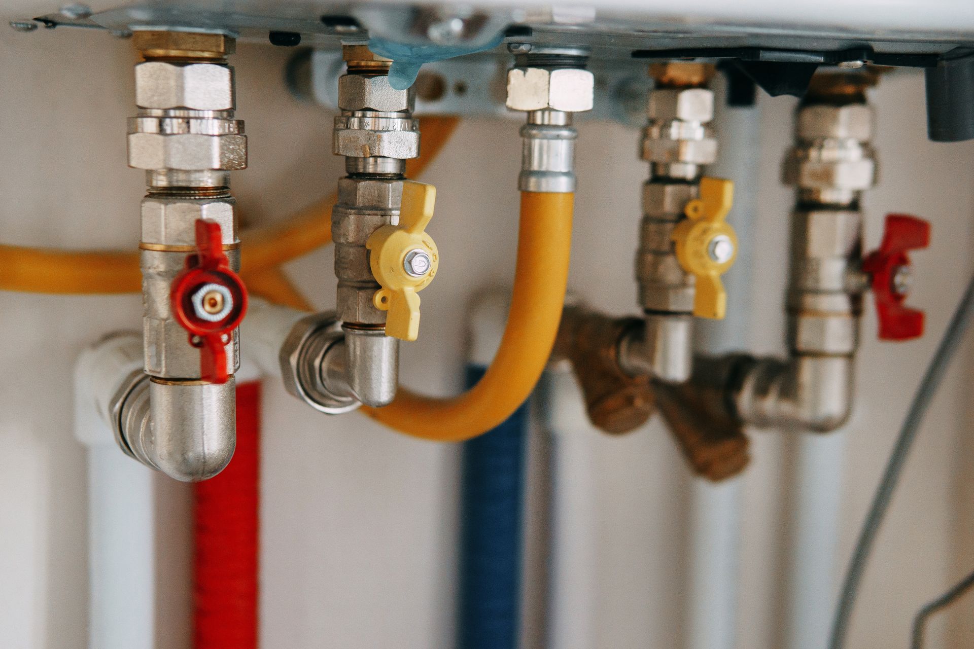 Plumbing pipes with red, yellow, and white valves and tubes against a white wall.