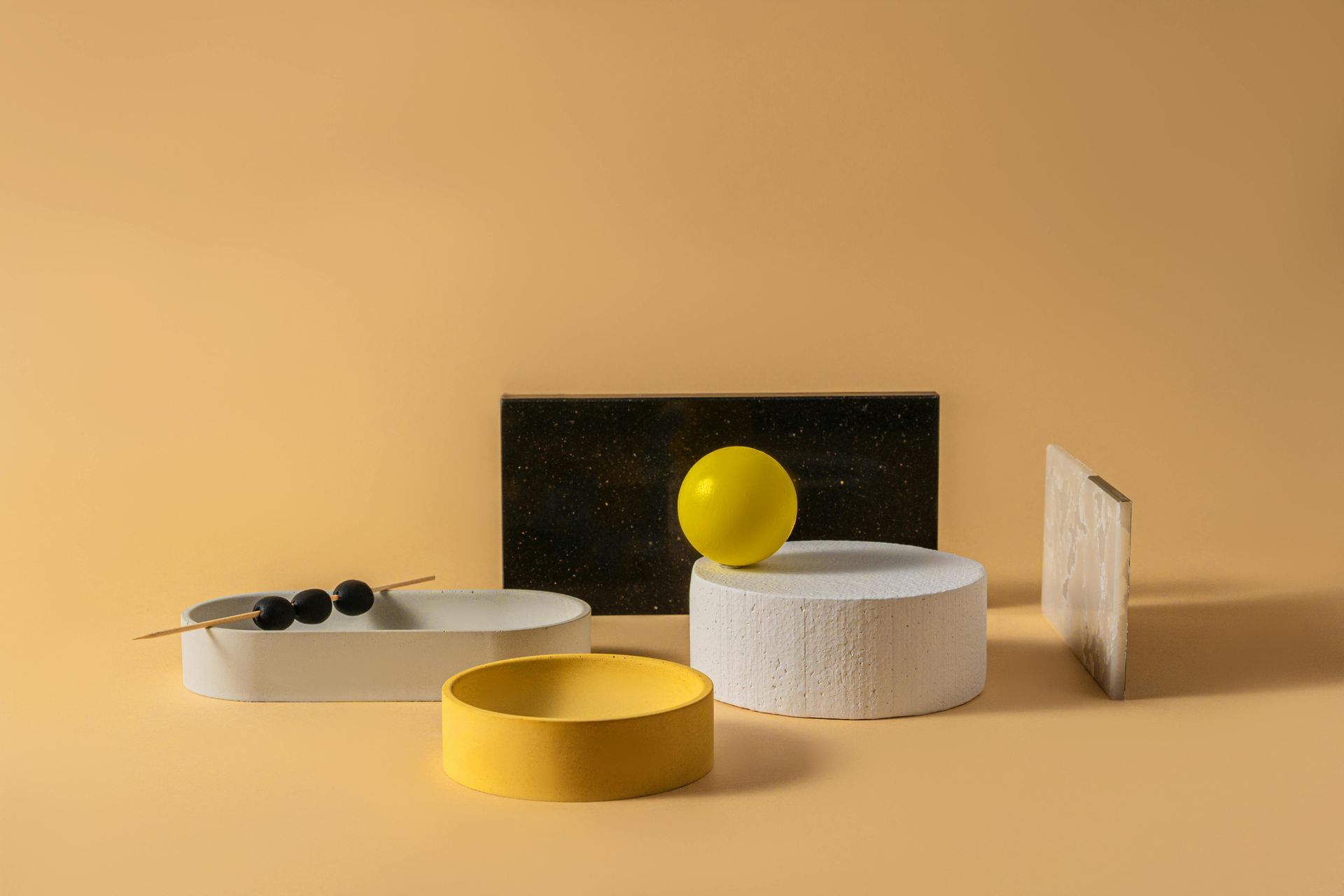 Abstract arrangement of geometric shapes and textures in shades of yellow, white, and black on a peach-colored background.
