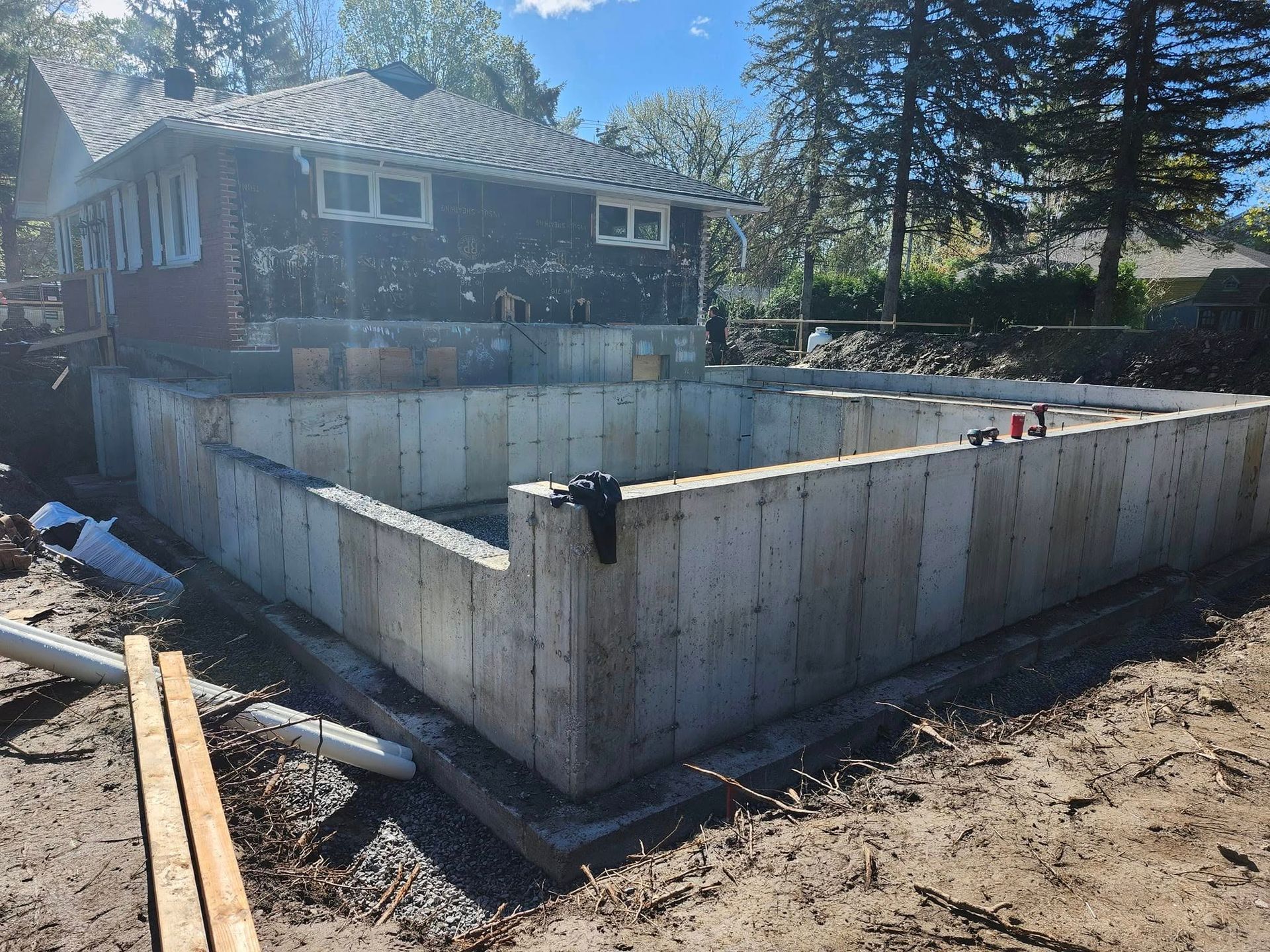 Fondations en béton pour une extension de maison en construction, situées devant une maison existante en rénovation.