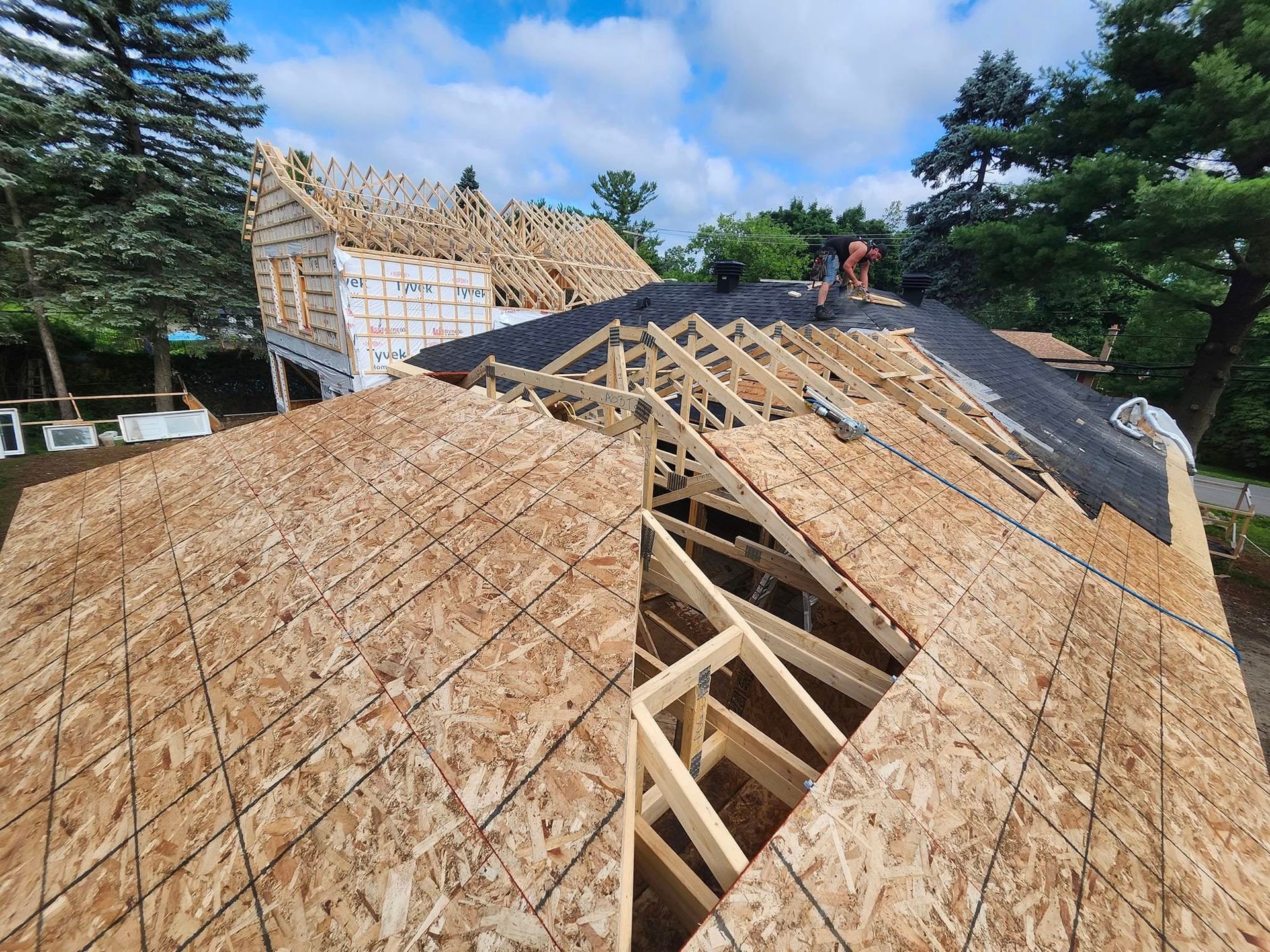Un ouvrier du bâtiment installe une sous-couche noire sur le toit à ossature bois d'une maison en construction.