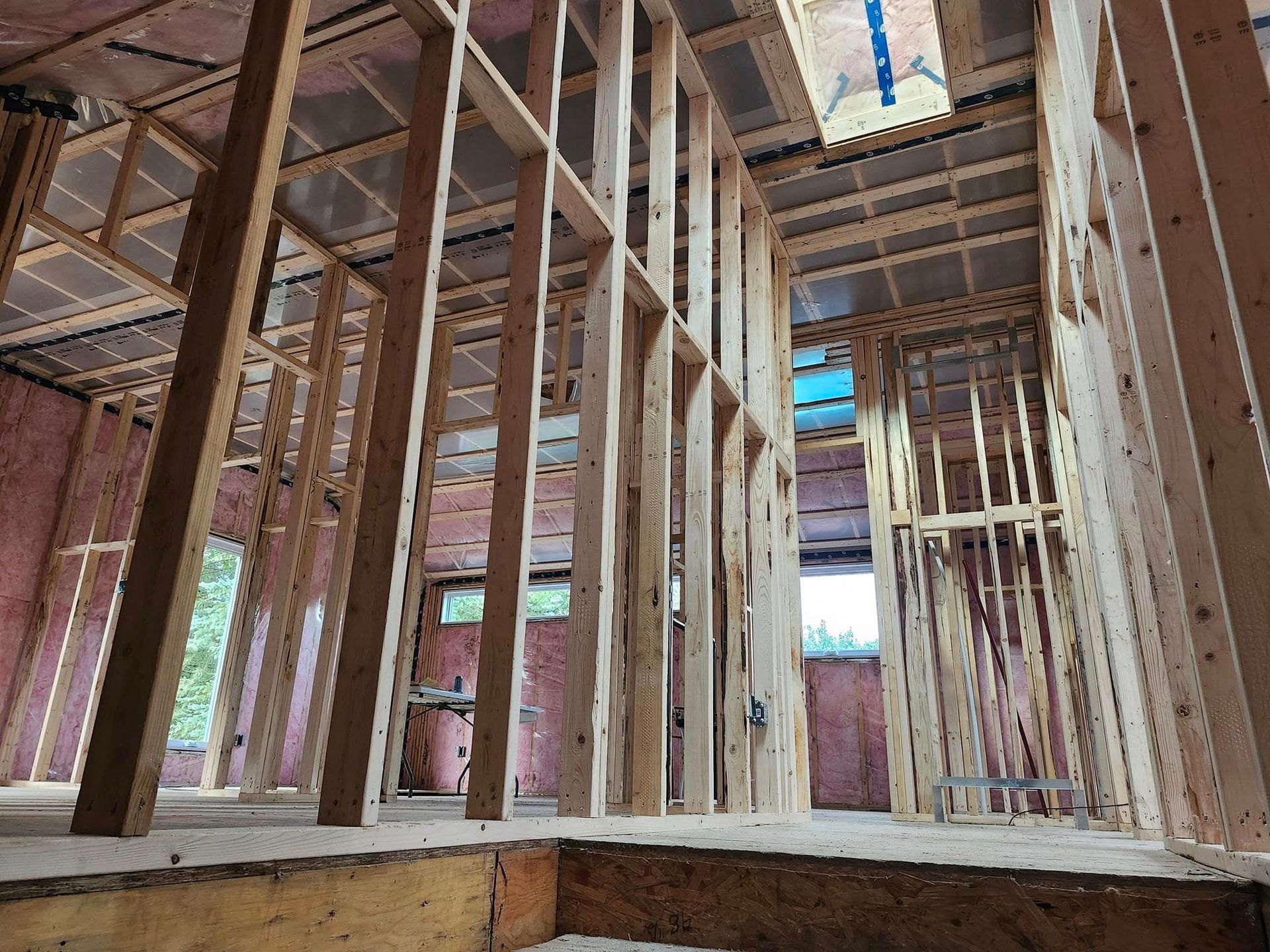 L'intérieur d'un bâtiment résidentiel en bois en construction, avec les montants muraux, les solives et l'isolation rose apparents.