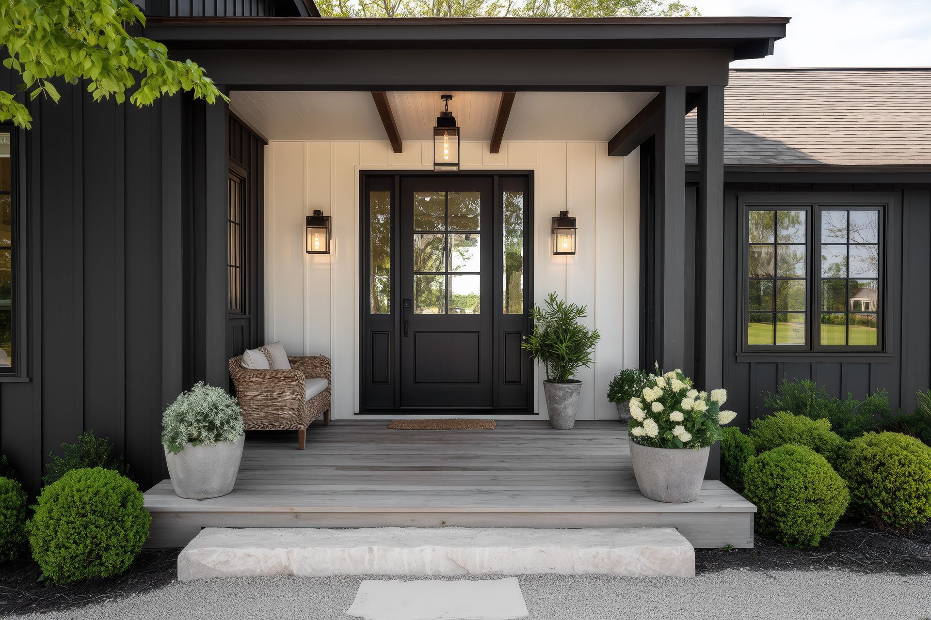 Entrée de style ferme moderne avec porte noire, bardage vertical blanc, porche végétalisé et marches en pierre.