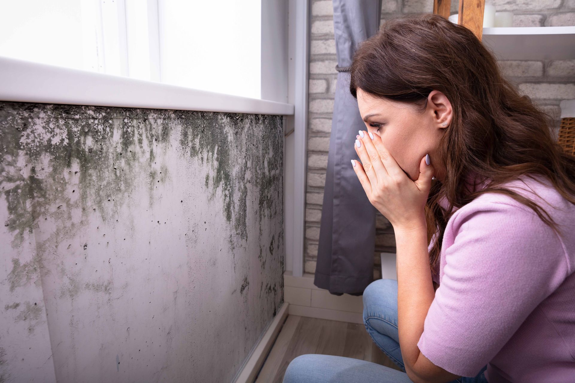 Une femme réagit à la présence de moisissures sur un mur de sa chambre. Elle se couvre le visage, l'air inquiet.