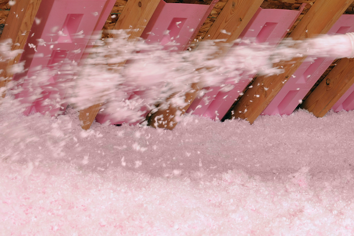 De l'isolant rose est insufflé dans un grenier, avec des panneaux de mousse rose insérés entre les poutres en bois.