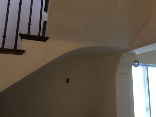An indoor view of a staircase with a curved drywall soffit, dark wood balusters, and a window with white trim.