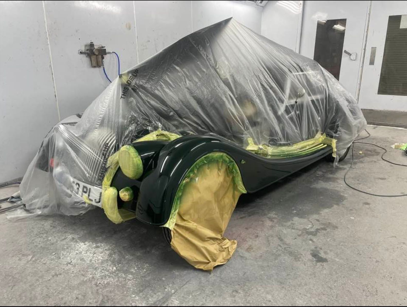 Morgan a car is covered in plastic wrap in a paint booth .