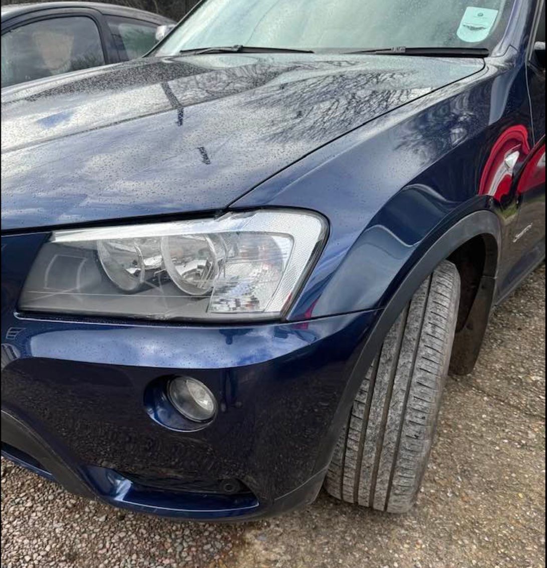 a blue car is parked on a gravel road .