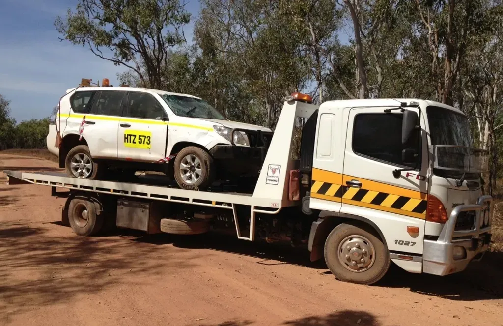 A white tow truck carrying a white Toyota Prado on its flatbed, parked on a dirt road in a forest. — Prompt Tilt Tray Towing & Recovery in Adelaide River, NT