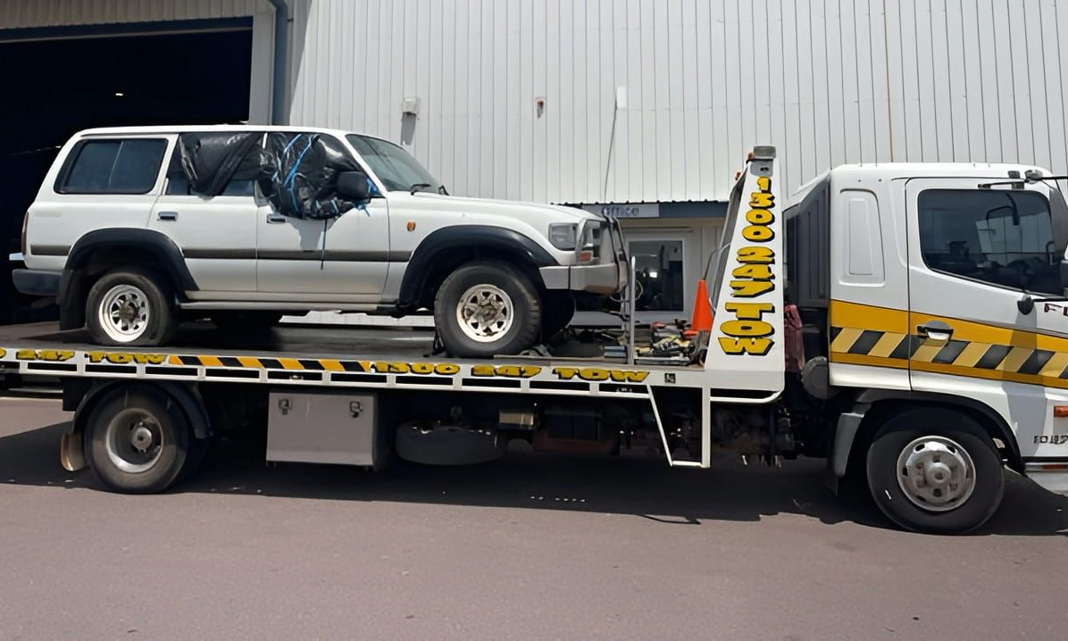 A white SUV being transported on a flatbed tow truck with yellow and black caution stripes. — Prompt Tilt Tray Towing & Recovery in Pine Creek, NT
