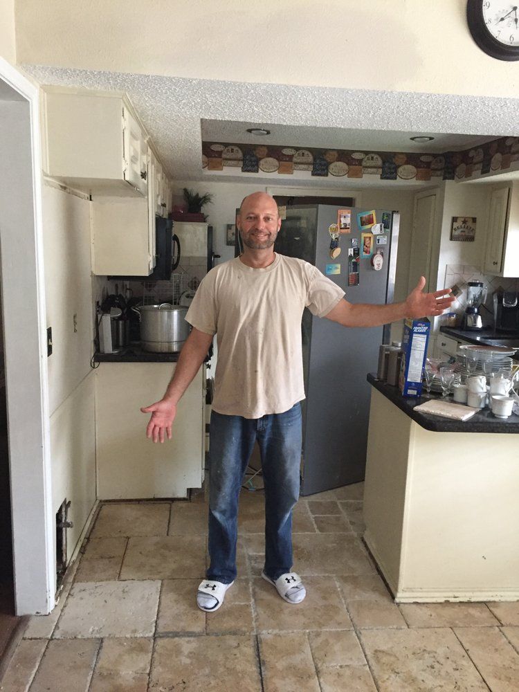 A man is standing in a kitchen with his arms outstretched.