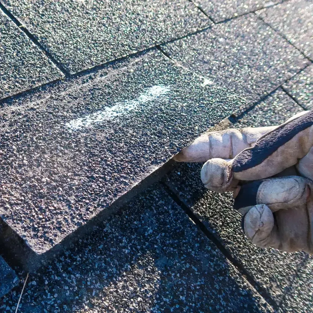 A person wearing gloves is holding a piece of shingles on a roof.