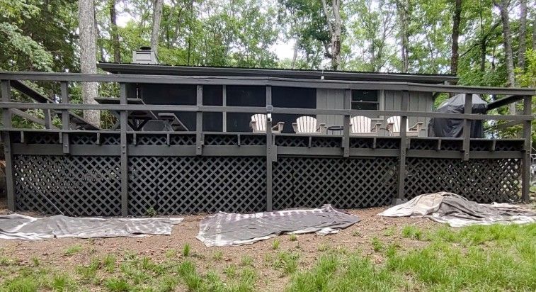 Dark house with black deck railing and white chairs on a wooded hillside
