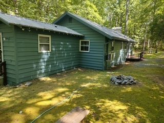 Green cabin in a wooded area with a metal roof and a small fire pit in the yard.