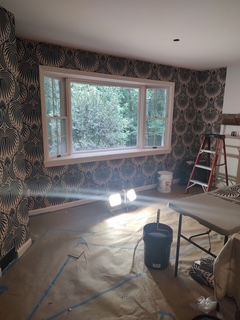 Living room under renovation with patterned wallpaper, window, ladder, and tools on covered floor.