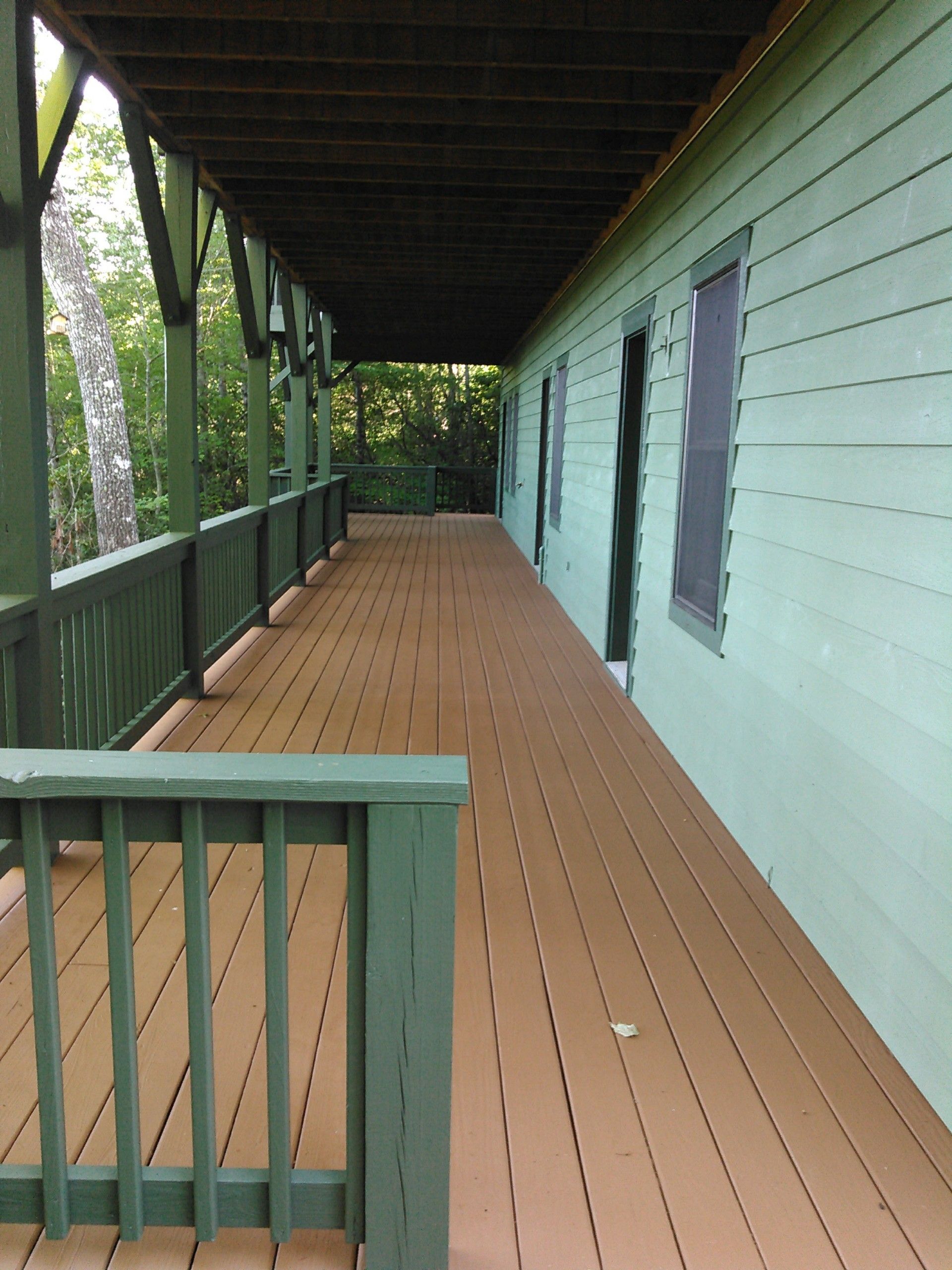 Covered porch with green railing and pale blue siding, featuring a wooden floor and open view outside