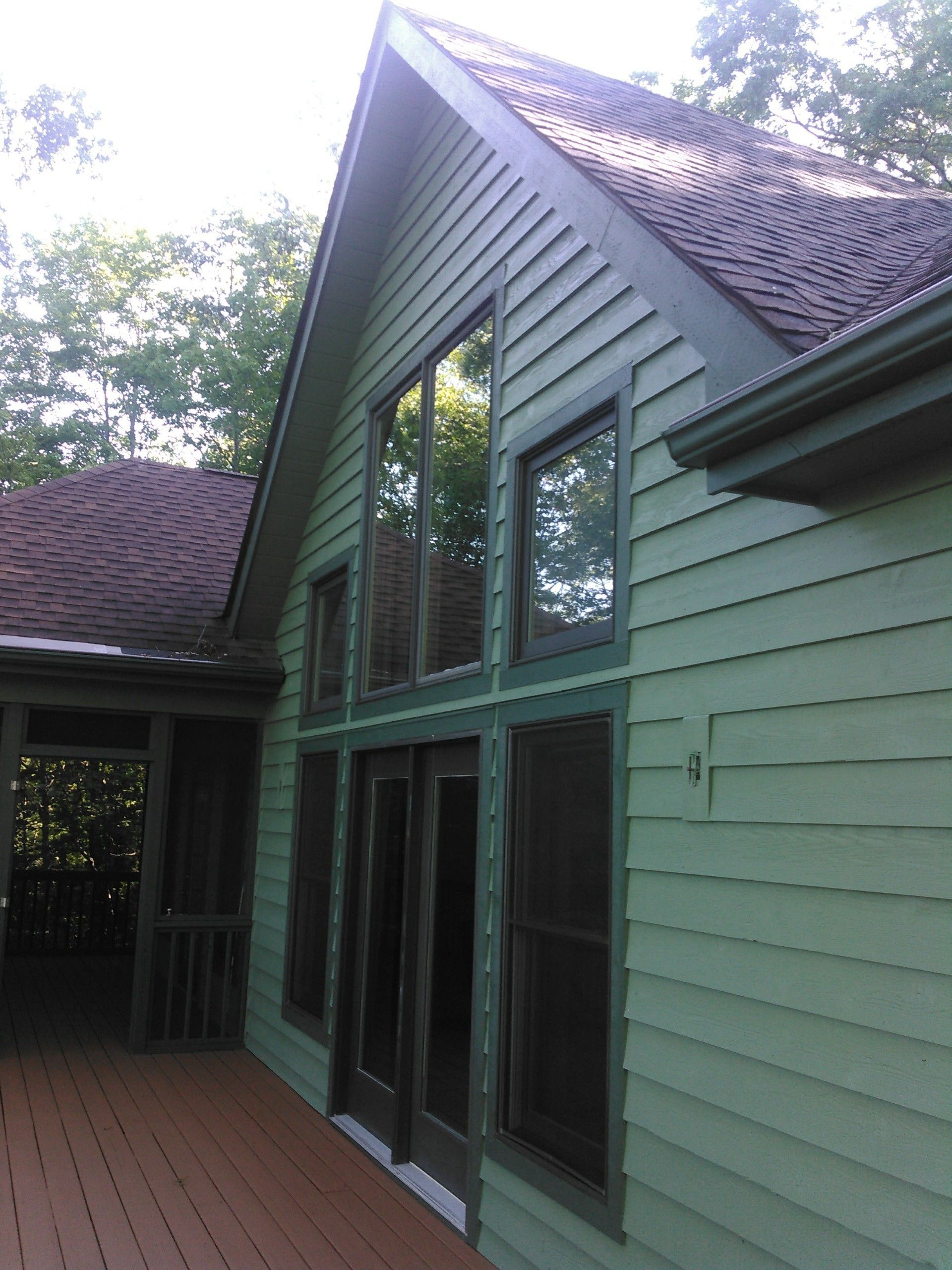 Modern house exterior with large windows, green siding, and a red shingled roof