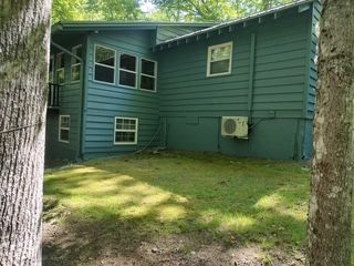 Green house exterior with small windows, an air conditioner, and a grassy yard shaded by trees