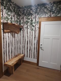Wood-paneled corner with birch tree wallpaper, a rustic bench, and a white door
