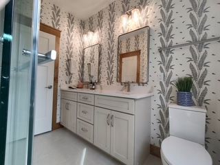 Bright bathroom with floral wallpaper, white vanity, and wall-mounted mirrors.