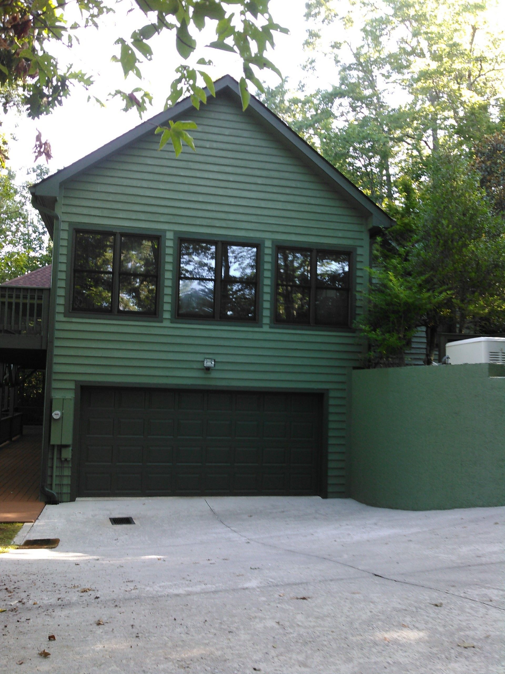 Green two-story house with garage and large front windows, viewed from the driveway
