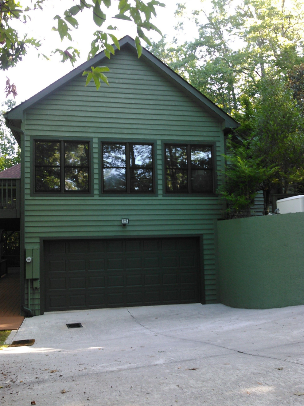 Green two-story house with a garage and large front windows under trees