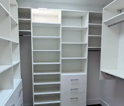 White built-in closet with shelves, drawers, and hanging rods. Well-lit, organized storage space.