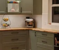 Green kitchen cabinets with wooden countertops and a silver toaster.
