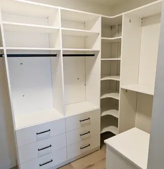 White walk-in closet with shelves, drawers, and hanging rods. Includes corner shelving unit and a white platform.