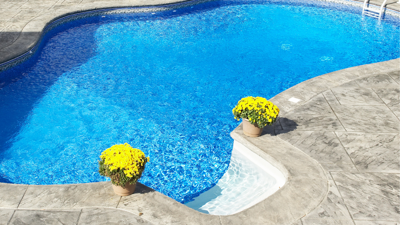 Backyard pool and spa with brick patio, tan house, and blue sky.