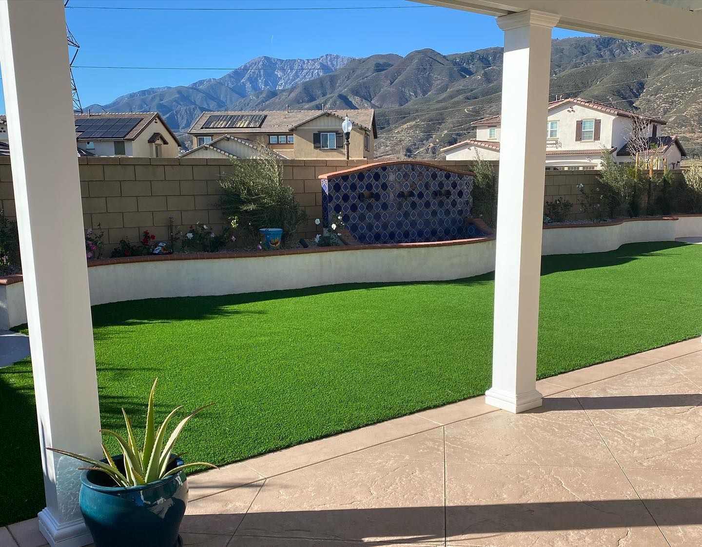 Covered patio overlooking a bright green backyard, with houses and mountains in the distance.