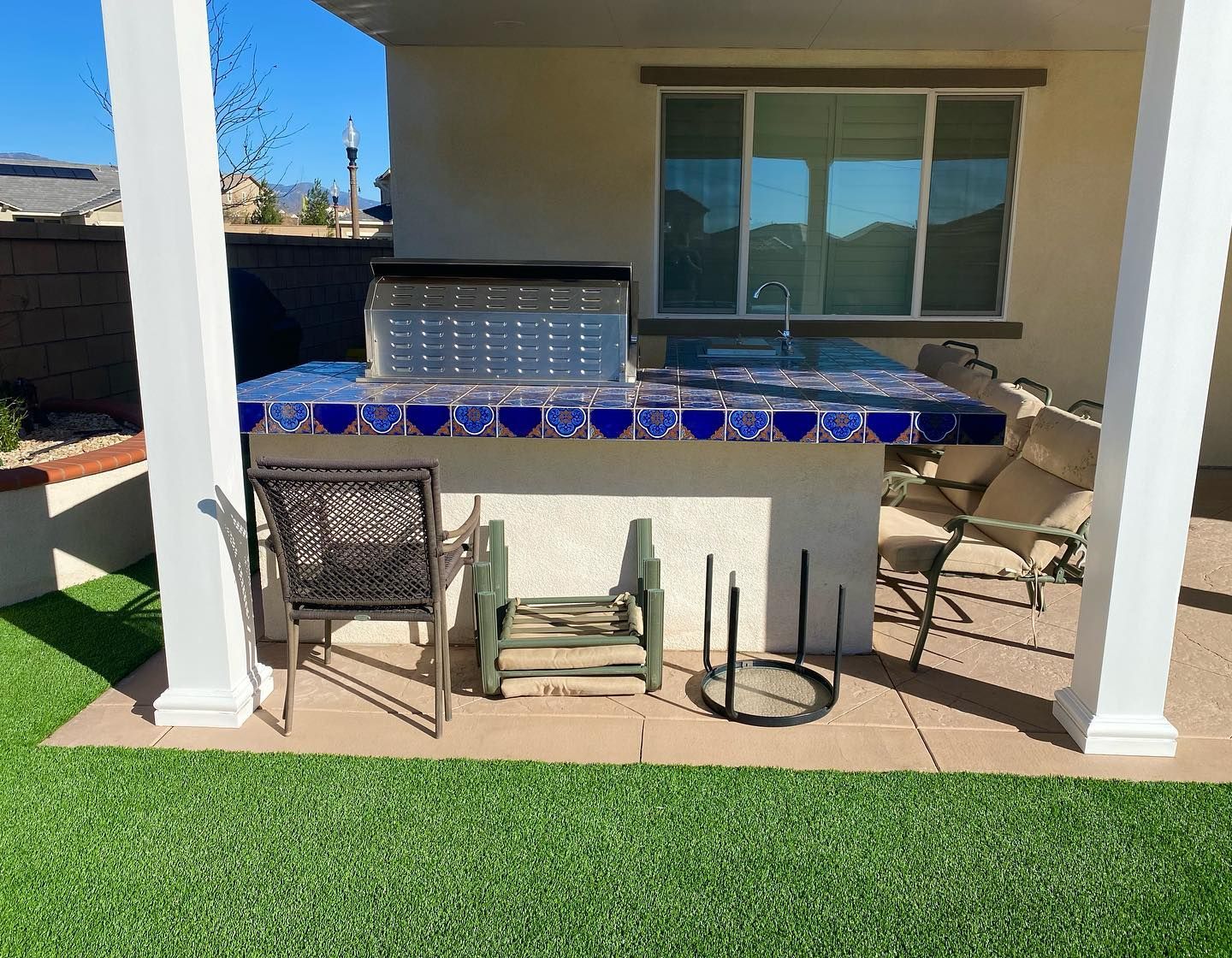 Covered patio with bar stools, blue tile counter, and artificial grass in a backyard