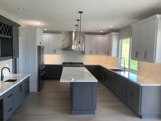 Modern kitchen with gray and white cabinets, large island, stainless hood, and wood floors.