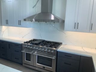 Modern kitchen with stainless steel stove and hood, white cabinets, and marble-look countertops