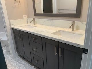 Modern bathroom vanity with dark cabinets, white double sink countertop, and large mirror