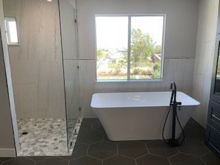 Modern bathroom with freestanding tub, walk-in shower, and large window overlooking greenery