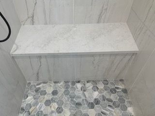 White marble-look shelf above hexagonal tile floor in a tiled shower area
