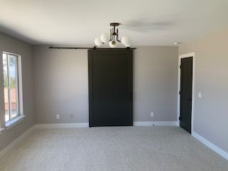 Empty gray bedroom with carpet, window, closet, and black door.