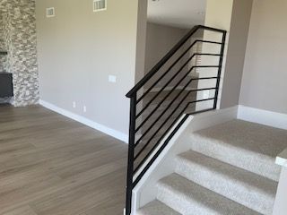 Carpeted staircase with black railing beside an open living room with wood flooring and stone fireplace