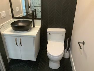 Small bathroom with wall-mounted sink, black basin, and toilet beside a towel bar and mirror.