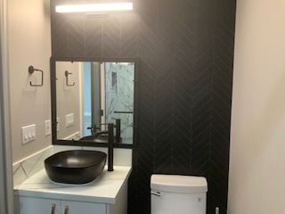 Modern bathroom vanity with black vessel sink, mirror, and toilet against a dark accent wall