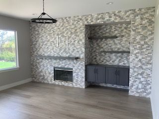 Modern living room with stone fireplace, built-in shelves, gray cabinets, and light wood floor