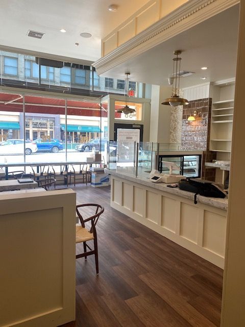 Bright café interior with white counter, wood floor, and large front windows overlooking the street