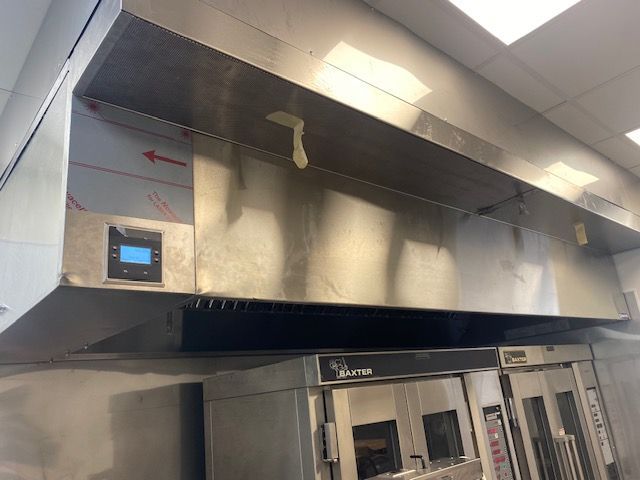 Stainless steel industrial kitchen hood with control panel above cooking equipment