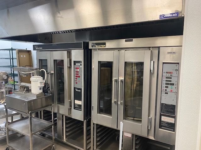 Large industrial oven in a stainless-steel commercial kitchen with a prep cart in front