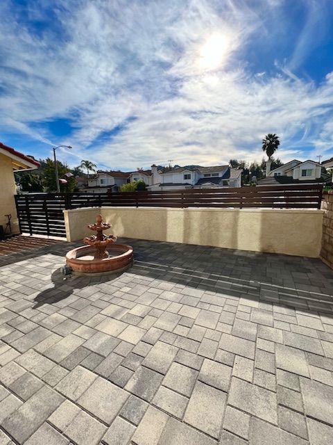 Sunny patio with gray pavers, a small fountain, and a cream wall overlooking a neighborhood skyline